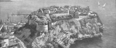 Blick über Monaco. General View of Monaco. This little independent principality sits on a huge rock with precipitous sides which juts out into the sea for 800 metres, and is 65 metres above the level of high water. A bridge connects rock and main-land. The territory formerly included Mentone and Rocca-bruna, but these were ceded to France in 1861 by Prince Charles III. The Palace is 15th century, the Cathedra modern.